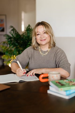 Agnieszka siedząca przy stole z notatnikiem i kolorowymi pomocami.